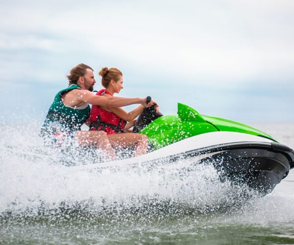 young people having fun driving on high speed on water scooter, man and woman on summer vacation, friends doing active sport